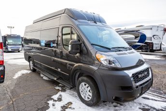 The image shows a black camper van parked on a lot. The van is likely a Ram model, featuring a high ...