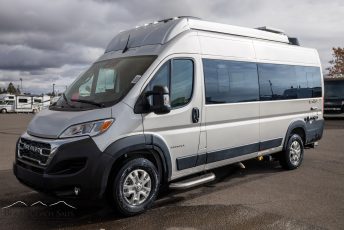 The image shows a silver van with a high roof, parked in an outdoor lot. The van appears to be a mod...