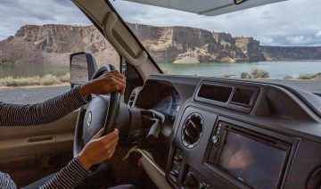 Driver's perspective from RV showing scenic lake and cliffs through windshield
