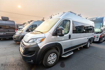 The image depicts a silver camper van parked among several other similar vehicles. The camper van is...