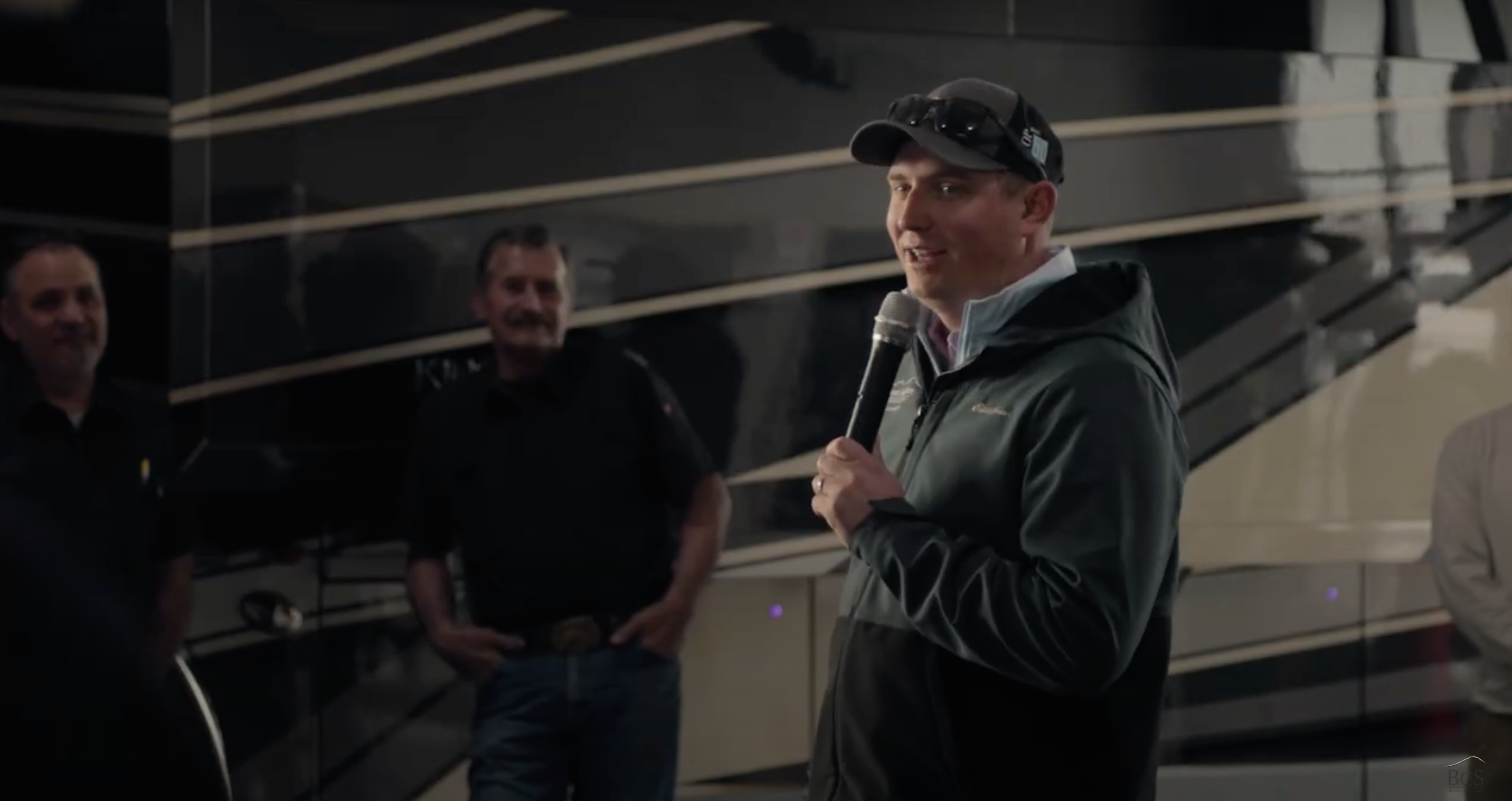 The image shows a group of people indoors, possibly in a workshop or presentation setting. One perso...