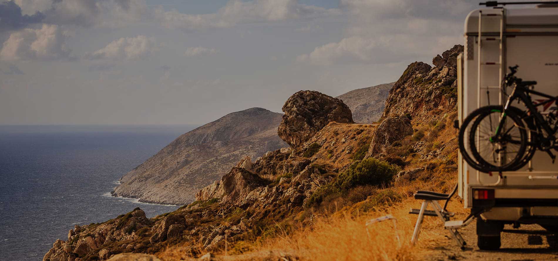 RV camping setup with bicycle and chair overlooking scenic coastal landscape at sunset